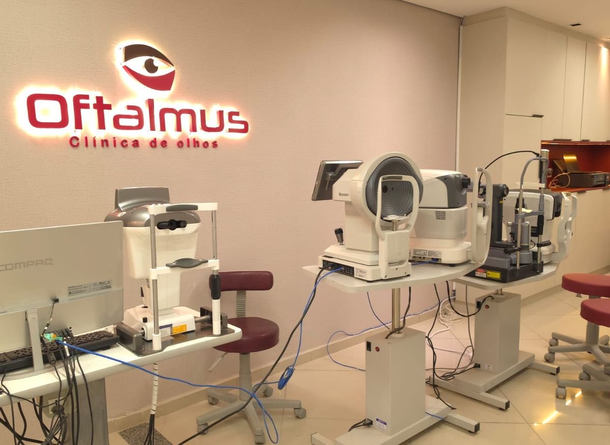 Sala de exames da Oftalmus, com os aparelhos e a logo da clínica na parede