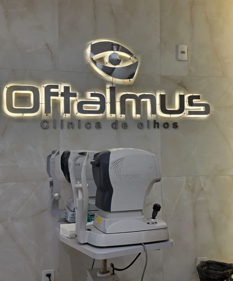 Logo da Oftalmus em metal na parede da clínica, atrás de um aparelho de exame